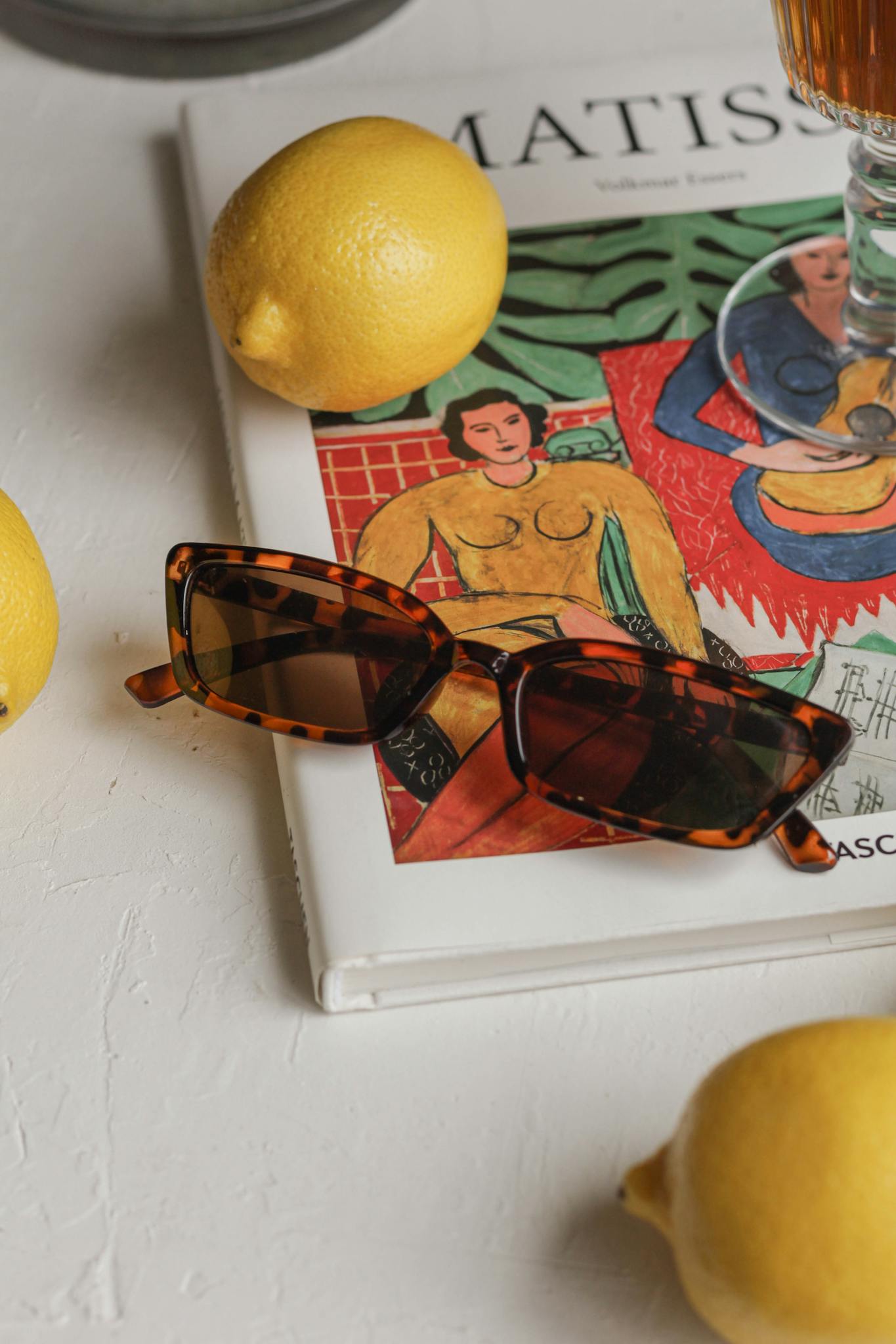 Artistic composition featuring sunglasses, lemons, and a Matisse art book on a white background.
